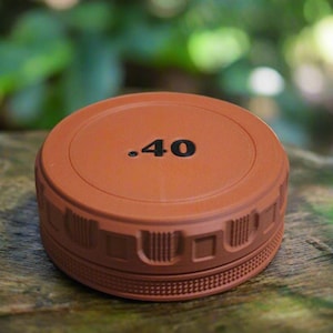May include: A round, terracotta-colored object with the number ".40" in black on the top. The object has a textured, patterned edge. The background is blurred, showing green foliage.