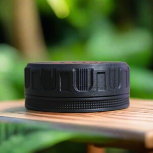 May include: A black, cylindrical object with a textured surface and a ridged design. The object is sitting on a wooden surface, with a blurred green background. The top of the object has a red detail.