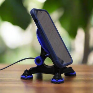 May include: A black and blue phone stand with a phone in a blue case. The stand has a tripod base with blue accents and a circular charging pad. A black cable extends from the stand.