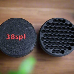May include: Two black, circular objects. One has the red text "38spl" on its top. The other has a wavy, honeycomb-like pattern. The objects are likely components of a larger item, possibly related to firearms or tools.
