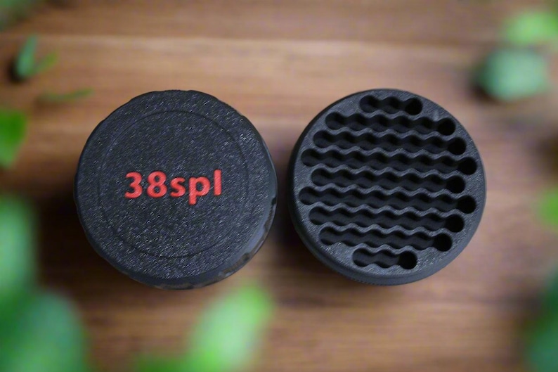 May include: Two black, circular objects. One has the red text "38spl" on its top. The other has a wavy, honeycomb-like pattern. The objects are likely components of a larger item, possibly related to firearms or tools.