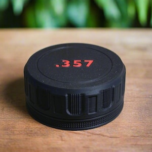 May include: A black, cylindrical object with the text ".357" in red. The object has a textured, ridged design around the sides. It is sitting on a wooden surface.