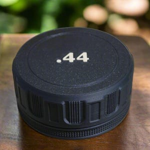 May include: A black, cylindrical object with the number ".44" in white text on top. The object has a textured surface and a ridged design around the sides. The item is sitting on a wooden surface.