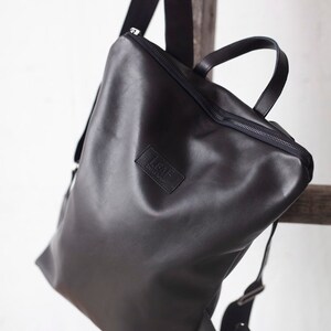 May include: A black leather backpack with a zipper closure and a small leather patch with the text "LEAF" on the front.