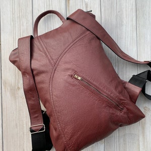 May include: A burgundy leather backpack with a zippered pocket on the front and adjustable straps. The backpack is made of a textured leather and has a casual style.