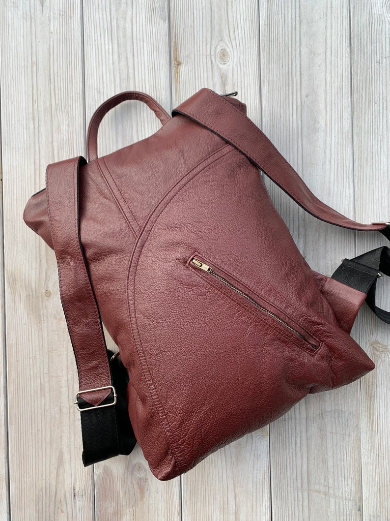 May include: A burgundy leather backpack with a zippered pocket on the front and adjustable straps. The backpack is made of a textured leather and has a casual style.