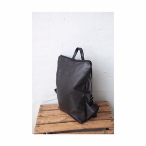 May include: A black leather backpack with a simple design. The backpack has a single zippered compartment and adjustable straps.