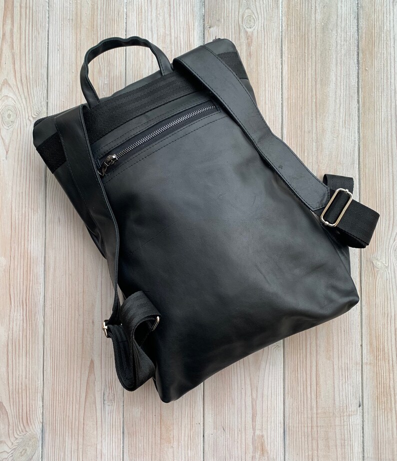May include: A black leather backpack with a zippered pocket on the front and adjustable straps.