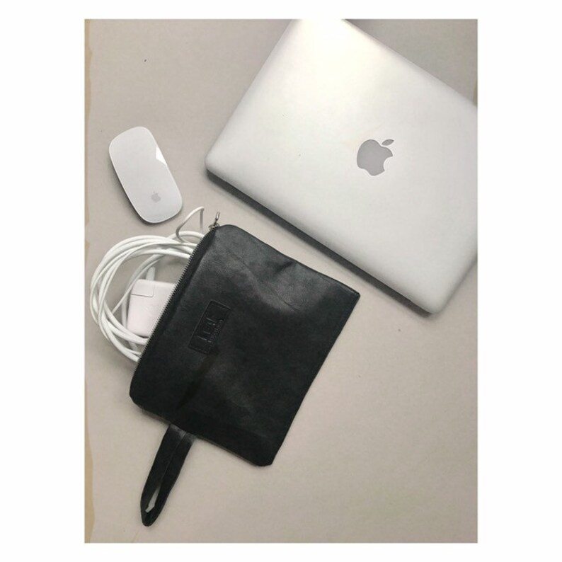 May include: A black leather pouch with a zipper closure and a handle. The pouch is lying on a white surface with a white mouse and a white laptop computer next to it. The laptop has an apple logo on the lid. The pouch has the word 'LIFT' embossed on it.