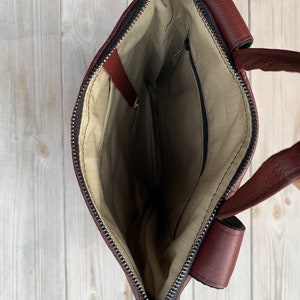 May include: The inside of a brown leather tote bag with a zipper closure. The bag has a small zippered pocket on the inside.