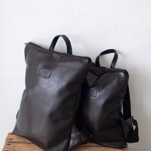 May include: Two black leather backpacks with zipper closures and adjustable straps. The larger backpack has the word "LEAF" printed on the front.