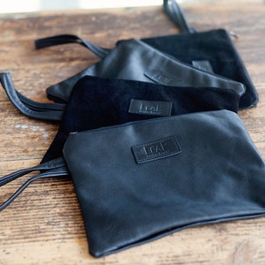 May include: Four black leather pouches with a zipper closure and a leather strap. Each pouch has a small rectangular label with the text "LEAF" and "Handmade" on it.