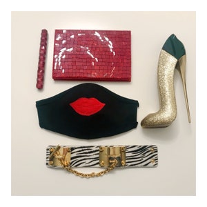 Op de afbeelding: Een zwart gezichtsmasker met een rood lippenontwerp, een rode glinsterende clutch, een gouden hoge hak schoen en een zebraprint armband met een gouden ketting.