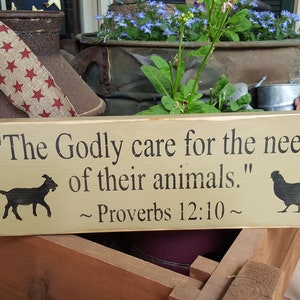 May include: A rustic wooden sign with the quote "The Godly care for the needs of their animals." Proverbs 12:10. The sign features a goat and chicken silhouette. The sign is light brown with black text.