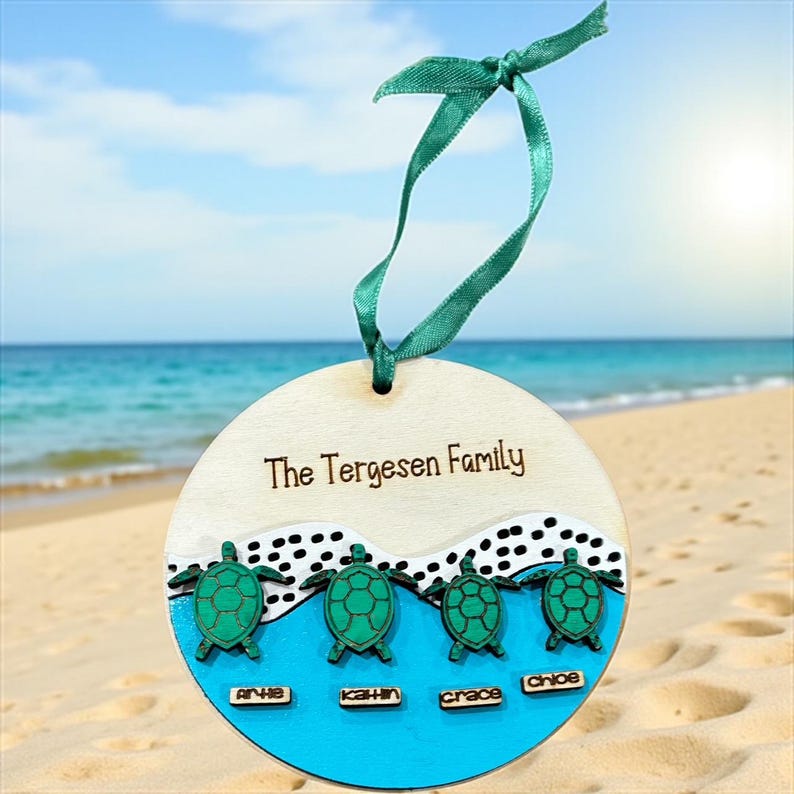 May include: A wooden family ornament with the text "The Tergesen Family". The ornament features four green sea turtles above the names Arha, Kahn, Grace, and Chloe. It has a teal ribbon for hanging.