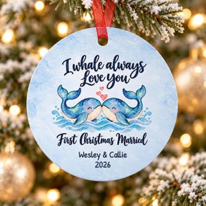 Puede incluir: Un adorno navide&ntilde;o redondo de cer&aacute;mica con un fondo de acuarela azul claro. Presenta dos ballenas azules toc&aacute;ndose las narices, tres peque&ntilde;os corazones rojos y el texto I whale always love you, First Christmas Married, Wesley & Callie, 2026.