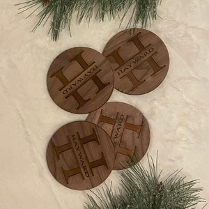May include: Four round wooden coasters with the name "Hayward" and the letter "H" engraved on each. The coasters are arranged in a circle on a white surface.