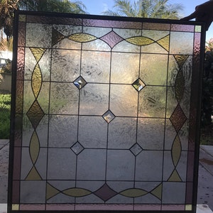 May include: A stained glass window with a geometric design featuring diamond shapes and curved lines. The glass is a mix of clear, frosted, and colored glass in shades of pink, yellow, and green.