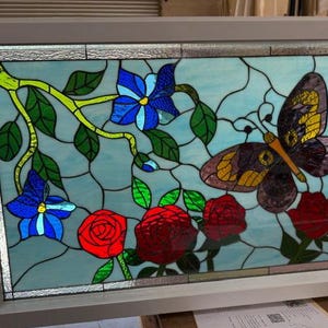 May include: A stained glass window depicting a butterfly with yellow and brown wings, perched on a branch with blue and red flowers. The background is a light blue sky.