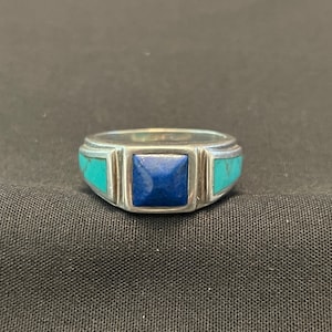 Puede incluir: Un anillo de plata con una piedra azul cuadrada y dos piedras turquesa a los lados.