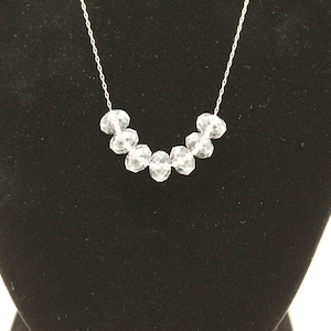 Puede incluir: Un collar de cadena de plata con una fila de cuentas de cristal facetadas transparentes.