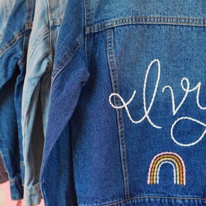 May include: A blue denim jacket with white embroidery that says "Ivy" and a rainbow below the name.