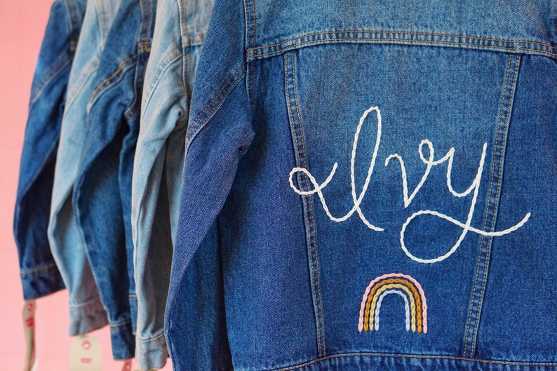 May include: A blue denim jacket with white embroidery that says "Ivy" and a rainbow below the name.