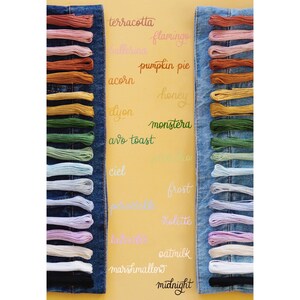 May include: A close-up of two denim panels with rows of embroidery floss in various colors. The floss is labeled with names like "terracotta", "flamingo", "pumpkin pie", "honey", "monstera", "avo toast", "ciel", "frost", "violette", "oatmilk", "marshmallow", and "midnight".