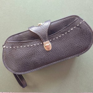 May include: A black leather clutch purse with a gold clasp and a white stitched design. The purse has a short strap.
