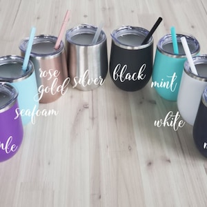 May include: A collection of insulated stemless wine tumblers in various colors, including purple, seafoam, rose gold, silver, black, mint, white, and navy. Each tumbler has a matching straw and the color name is written on the side.