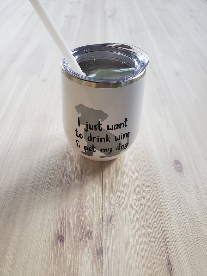 May include: White insulated wine tumbler with a clear lid and a white straw. The tumbler features a gray silhouette of a dog and the text "I just want to drink wine & pet my dog" in black. The tumbler is designed for cold beverages.