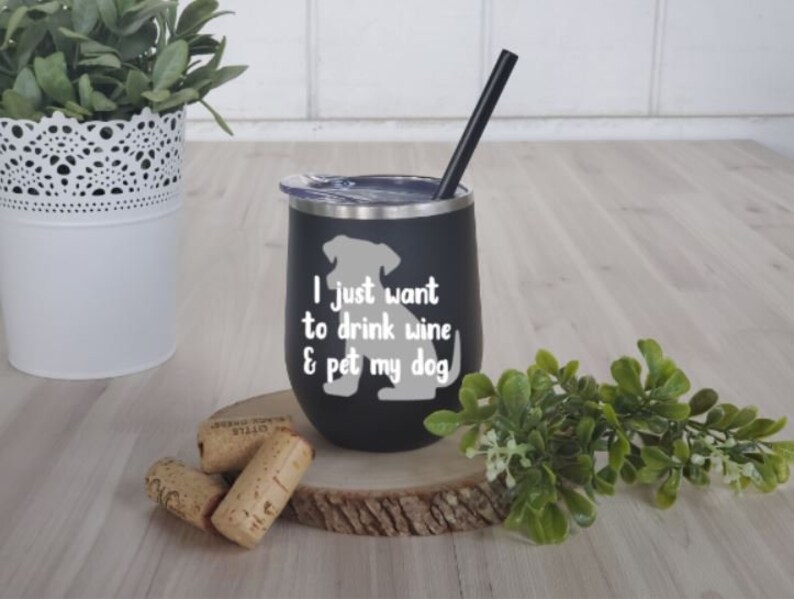 May include: Black insulated wine tumbler with a silver rim and a black straw. The tumbler has a white graphic of a dog and the text "I just want to drink wine & pet my dog."