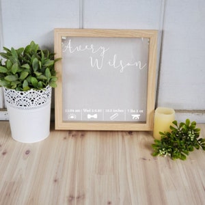 K&ouml;nnte beinhalten: Ein Holzrahmen mit wei&szlig;em Hintergrund und einer durchsichtigen Vorderseite. Der Rahmen enth&auml;lt eine wei&szlig;e Inschrift mit dem Text "Avery Wilson" und die Geburtsdaten des Babys: 11:34 Uhr, Mi 5.6.20, 18,5 Zoll, 7 Pfund 5 Unzen. Der Rahmen steht auf einer hellbraunen Holzoberfl&auml;che.