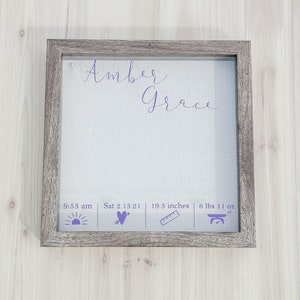 K&ouml;nnte beinhalten: Ein gerahmter Druck mit dem Namen "Amber Grace" in lilafarbener Kursivschrift. Der Druck enth&auml;lt auch die Geburtszeit, das Datum, die L&auml;nge und das Gewicht des Babys. Der Rahmen ist aus Holz mit einer hellbraunen Oberfl&auml;che.