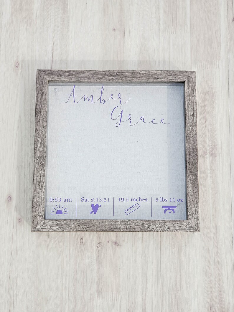 K&ouml;nnte beinhalten: Ein gerahmter Druck mit dem Namen "Amber Grace" in lilafarbener Kursivschrift. Der Druck enth&auml;lt auch die Geburtszeit, das Datum, die L&auml;nge und das Gewicht des Babys. Der Rahmen ist aus Holz mit einer hellbraunen Oberfl&auml;che.