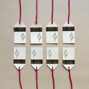May include: Eight white gift tags with red and green plaid ribbon and a cut-out ornament design. The tags are tied with red string.