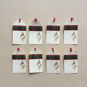 May include: Eight white gift tags with red and green plaid ribbon and a cut-out ornament shape.