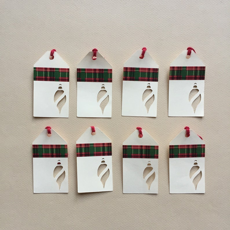 May include: Eight white gift tags with red and green plaid ribbon and a cut-out ornament shape.