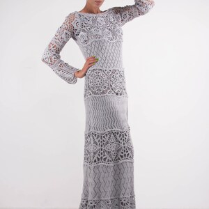 May include: A long, gray crochet dress with a loose fit and a scalloped hem. The dress has a variety of crochet patterns throughout, including floral and geometric designs.