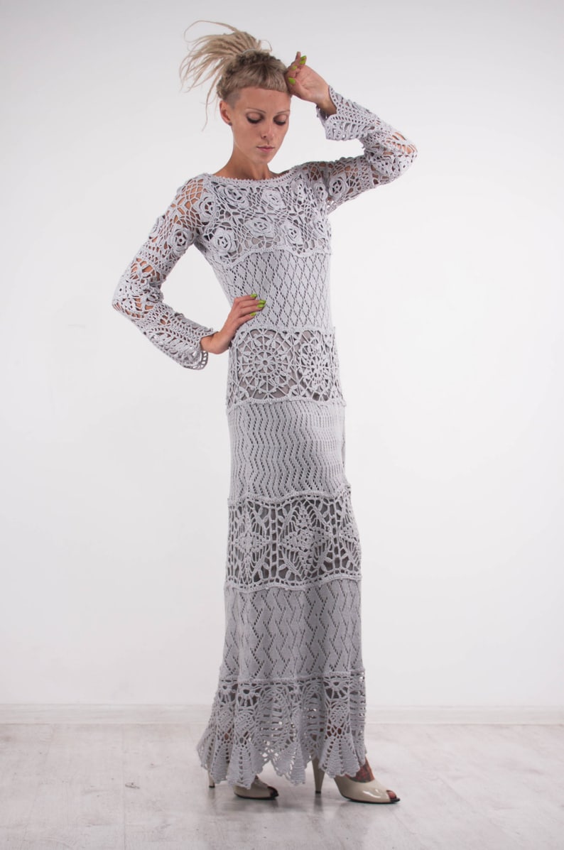 May include: A long, gray crochet dress with a loose fit and a scalloped hem. The dress has a variety of crochet patterns throughout, including floral and geometric designs.