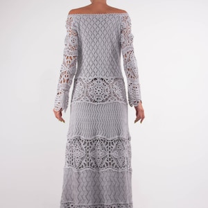 May include: A gray crochet maxi dress with a long-sleeved off-the-shoulder design. The dress features a delicate floral pattern and a tiered skirt.