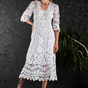 May include: A white crochet maxi dress with a scalloped hem and three-quarter sleeves. The dress is made of delicate lace and has a loose, flowing fit.