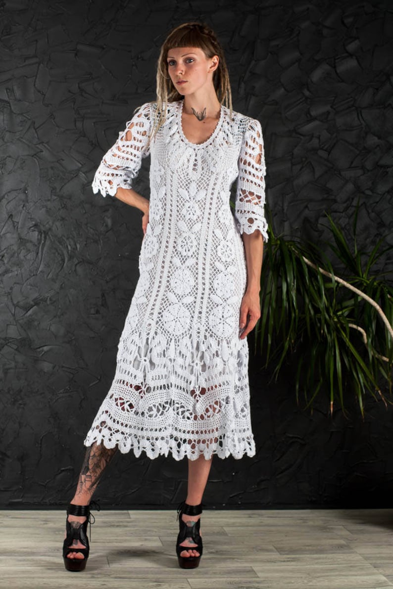 May include: A white crochet maxi dress with a scalloped hem and three-quarter sleeves. The dress is made of delicate lace and has a loose, flowing fit.