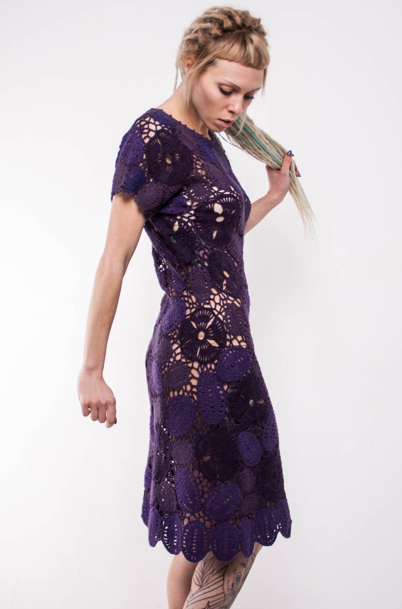 May include: A purple crochet dress with a floral pattern. The dress is sleeveless and has a fitted bodice. The skirt is full and flows to the knees.