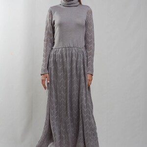 May include: A gray knitted maxi dress with a turtleneck and a chevron pattern. The dress has long sleeves and a fitted bodice.