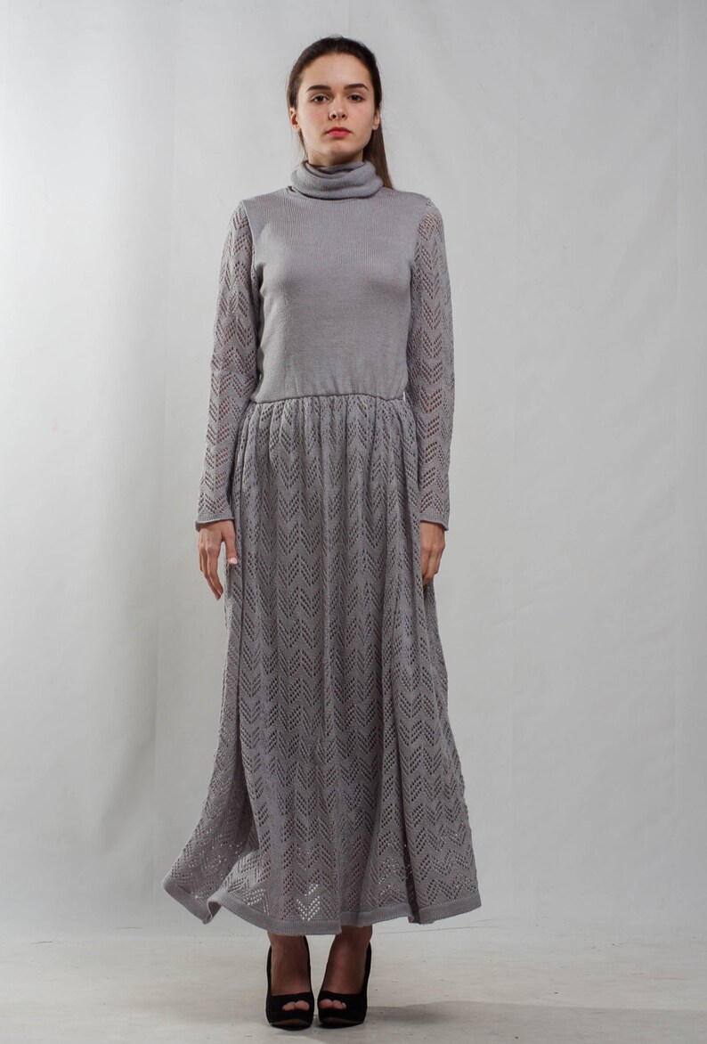 May include: A gray knitted maxi dress with a turtleneck and a chevron pattern. The dress has long sleeves and a fitted bodice.