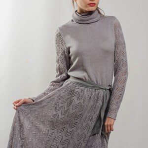 May include: A gray knitted dress with a long skirt and a turtleneck. The dress has a delicate lace pattern and a matching gray belt.
