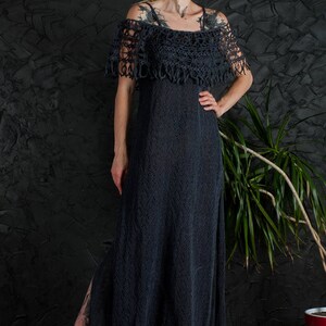 May include: A long, dark gray crochet dress with a crocheted off-the-shoulder neckline and a slit up the side. The dress is worn by a person with tattoos and dreadlocks.