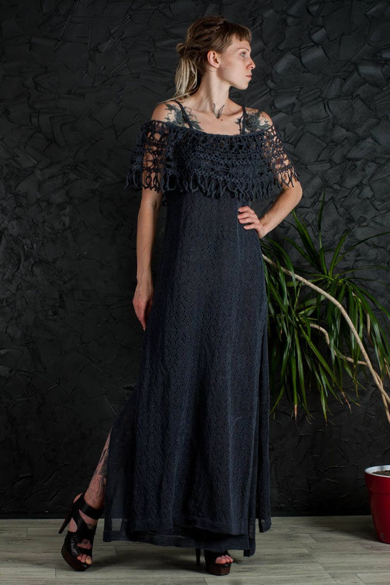 May include: A long, dark gray crochet dress with a crocheted off-the-shoulder neckline and a slit up the side. The dress is worn by a person with tattoos and dreadlocks.