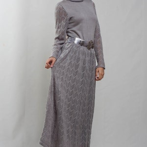 May include: A gray knitted maxi dress with a turtleneck and a silver belt. The dress has a chevron pattern and is worn by a person with dark hair.